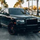 Front and side view of a black 2024 Rolls-Royce Cullinan SUV with custom Forgiato wheels, parked on a city street.
